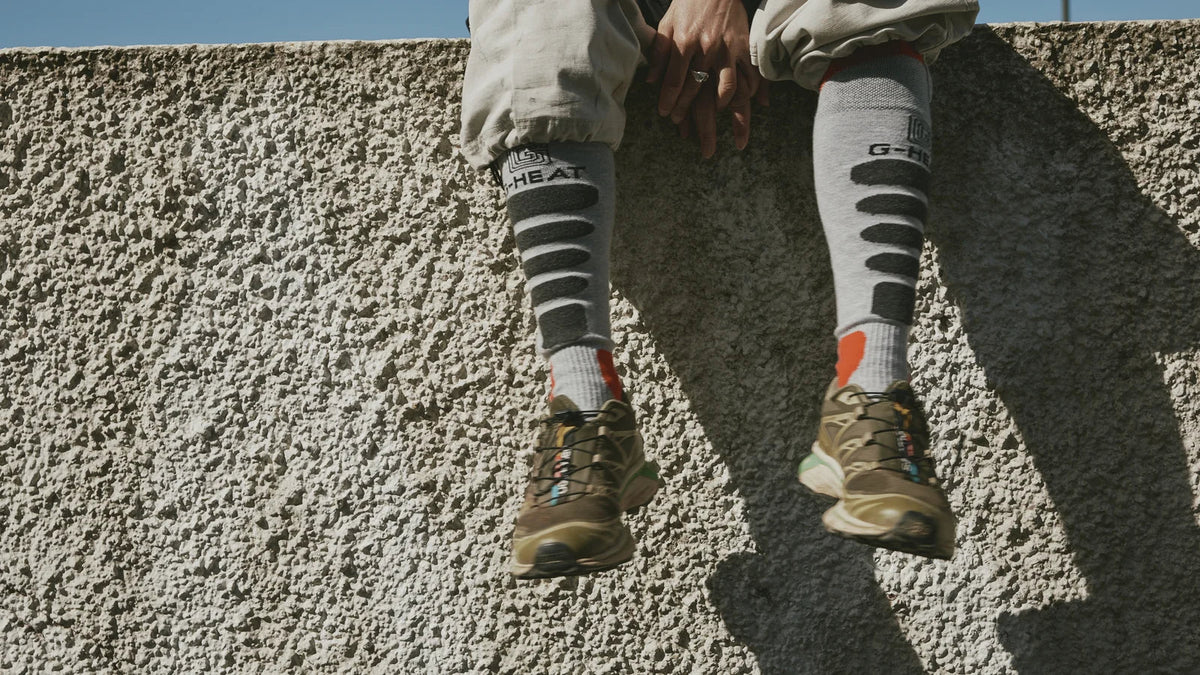 graue beheizbare Socken von G-HEAT mit Trailschuhen auf einer Mauer