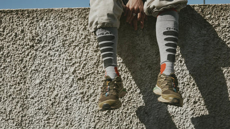 graue beheizbare Socken von G-HEAT mit Trailschuhen auf einer Mauer