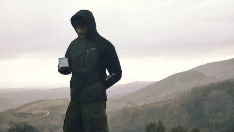 Wanderer in Kapuzenjacke mit einer Tasse in der Hand vor nebligen Hügeln